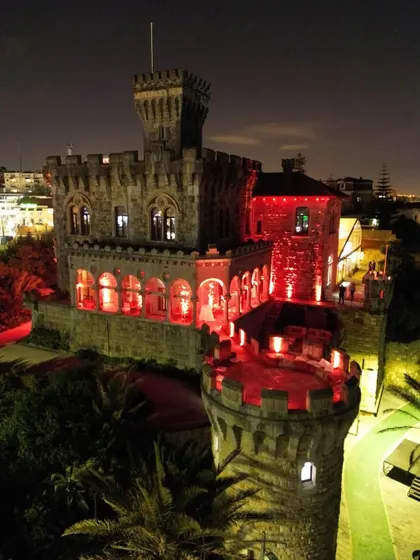 The same Lisbon castle lit up in dramatic red at night. This demonstrates how we use architectural lighting to completely transform a venue's mood from day to night for the reception party.