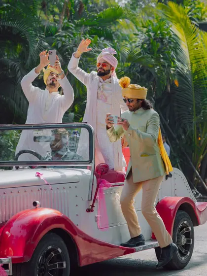 The groom's friends having fun during the baraat, taking pictures from a vintage car.