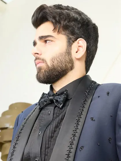 A close-up profile view of the navy blue tuxedo, highlighting the intricate beadwork on the lapel and the sharp tailoring around the collar and shoulders.