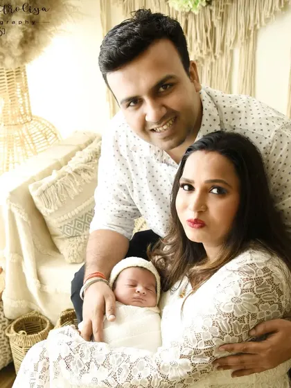 A relaxed family portrait in a bohemian-styled studio setup. The family is seated together, smiling for the camera, showcasing a more casual and lifestyle approach to newborn photography.