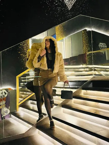 A fun and stylish look featuring a sheer top, cargo skirt, and a cozy fur hoodie, playing with reflections on a mirrored staircase.