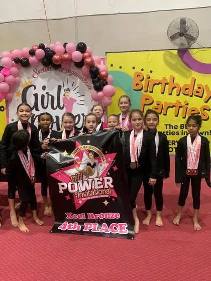 Our Xcel Bronze team proudly displays their 4th place banner at the Svetlana Boguinskaia Invitational.