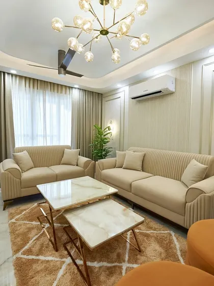 This living room uses a calm, neutral palette of white and beige, with a striking chandelier and a nested marble coffee table as the centerpiece. The fluted wall panels add a modern, textural element.