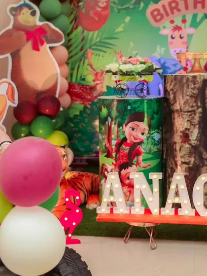 A wild jungle adventure for a first birthday. This setup includes a lush green backdrop with characters from The Lion King and Mighty Little Bheem, complete with a mini jeep for the birthday girl to explore in.
