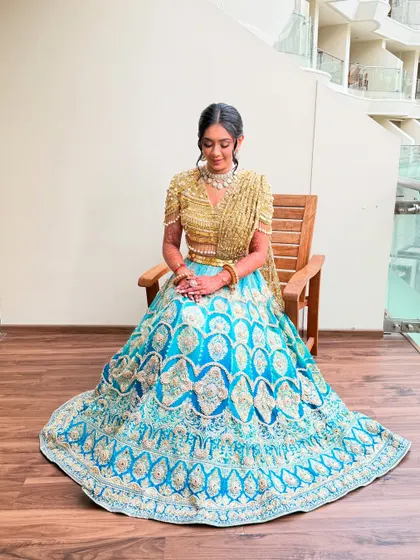 A full-length portrait of the bride seated, her blue and gold lehenga spread out in all its glory.
