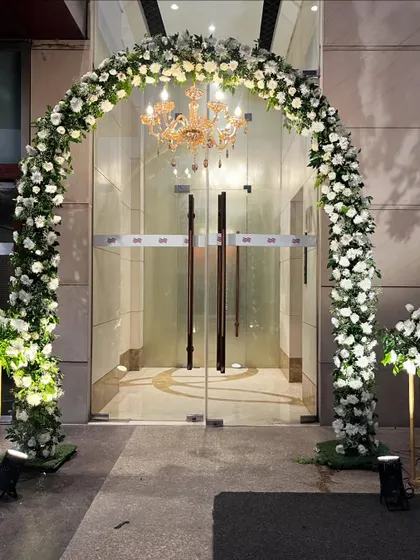A beautiful floral arch at the main door of the venue. This elegant arrangement of white roses and a classic chandelier provides a warm and luxurious welcome to guests.