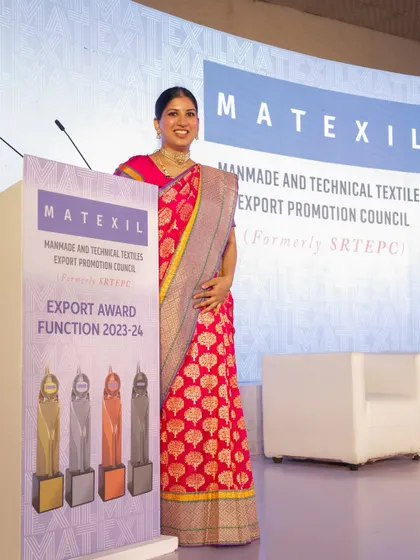 A portrait by the podium at the MATEXIL awards, dressed in a traditional saree to match the formal and prestigious nature of the event.