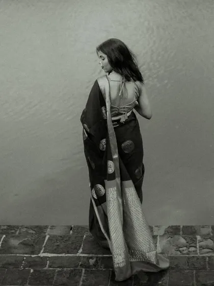 A full-length back profile in black and white. This artistic shot focuses on the silhouette and the beautiful drape of the saree against a minimalist background, emphasizing form and texture.