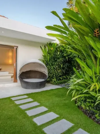 A private outdoor seating area connected to a bedroom, featuring a perfect lawn and a simple stone path. The surrounding tall, leafy plants provide privacy and a sense of enclosure.