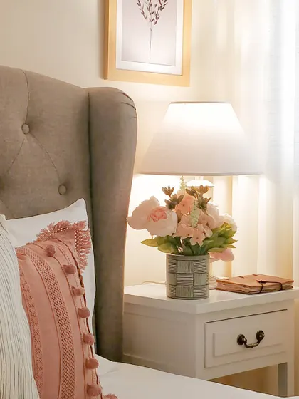 A close-up of the bedside vignette. The shape of the lamp, the soft floral arrangement, and the textured pillows come together to create a calm and collected moment in this cozy bedroom.