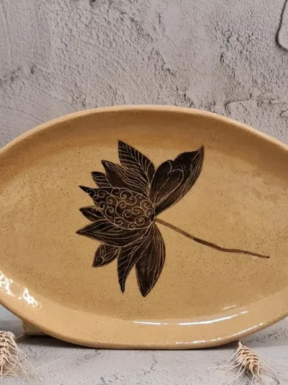 This organic, oval-shaped plate features a single, beautifully detailed lotus flower. It's a versatile piece that can be used for serving scones, sushi, or simply as a decorative item in your home.