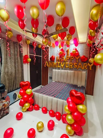 A classic red and gold anniversary room decoration. The setup includes 'Happy Anniversary' foil letters, and red and gold balloons on the ceiling and floor.
