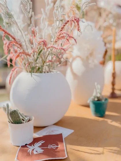 A close-up of the delicate table decor, featuring white vases with pink-tinged dried flowers and small cacti, adding a subtle touch of color to the neutral theme.