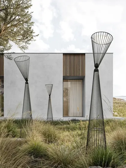 A group of Ikonika floor lamps of different sizes is arranged in an outdoor landscape, appearing like sculptural totems in the wild grass.