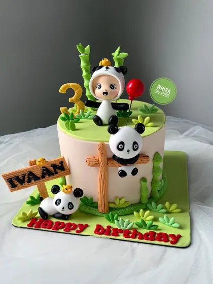An adorable panda-themed cake for a third birthday. This design features a child in a panda costume surrounded by cute, handcrafted panda friends and bamboo details.