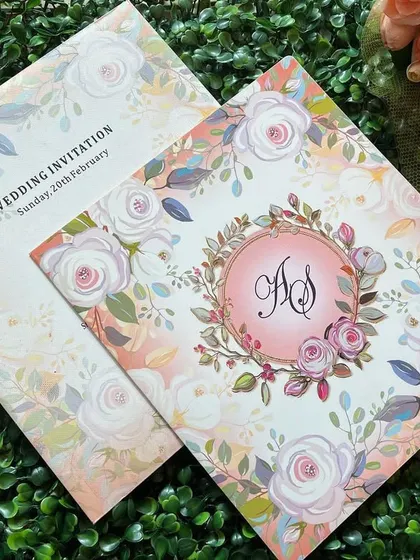 A closer look at a custom floral wedding invitation. The design features a personalized monogram with the couple's initials set within a beautiful watercolor floral wreath.