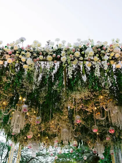 A canopy of lush greenery and baby's breath, with crystal chandeliers and floral-filled glass orbs hanging down, creating a magical, enchanted garden ceiling.