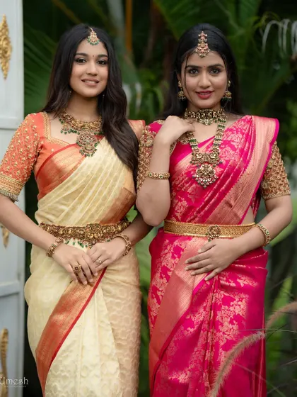 A beautiful portrait of two models wearing our traditional antique sets. One features a cream and red combination, while the other is in vibrant pink, showing the versatility of our collection.
