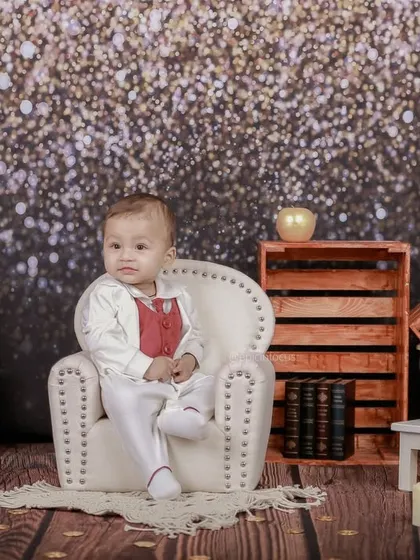 Dressed in a smart white and red suit, this baby sits like a little gentleman against a sparkling glitter backdrop, creating a glamorous and celebratory portrait.
