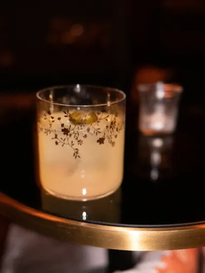 A classic cocktail in an ornate glass, shot with low light. The focus is on the elegant glassware and the warm, intimate ambiance of the bar.