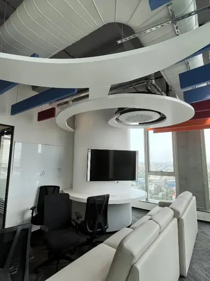 An informal meeting lounge at Kissflow with a comfortable sofa and stunning views of the city. The sculptural ceiling element and modern furniture create a sophisticated yet relaxed atmosphere for client meetings or team discussions.
