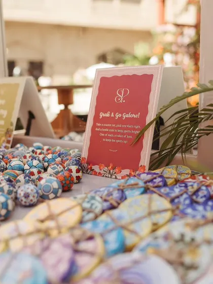 A 'Grab & Go Galore' station at a Parisian-themed Mehendi, featuring hand-painted ceramic knobs and cookies as unique, artistic favors for guests to take home.