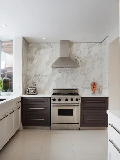 This kitchen design uses a stunning marble-patterned backsplash as a focal point. The mix of dark lower cabinets and white upper cabinets creates a balanced and sophisticated look.