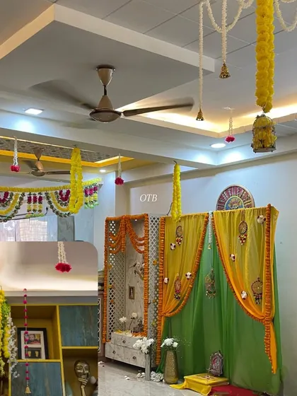 A combined look at the home decoration, showing the decorated pooja mandap and the floral hangings from the ceiling that tie the whole space together.