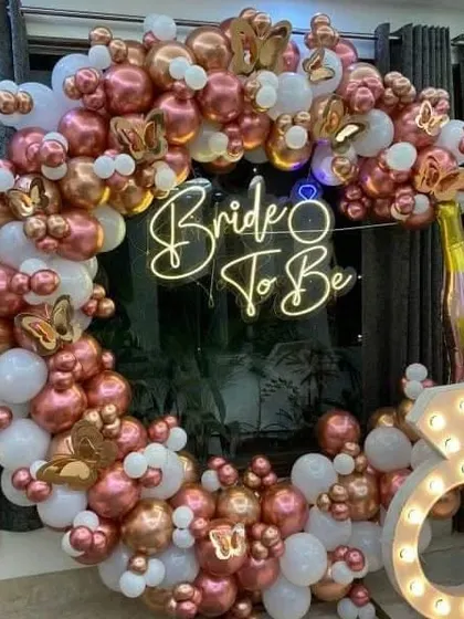 For a modern bridal shower, I put together this glamorous photo booth. It features a full ring of rose gold and white balloons, a custom 'Bride to Be' neon sign, and a large marquee light in the shape of a diamond ring for that extra sparkle.