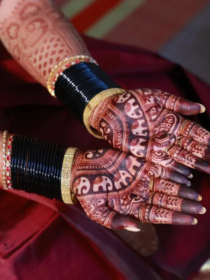 A close-up of a rich, dark henna stain on the palms, paired with traditional black bangles. The contrast makes the elephant designs stand out beautifully.