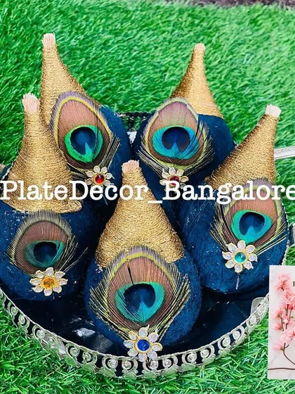 A set of five coconuts decorated with royal blue velvet, gold thread, and natural peacock feathers, presented in a silver tray for an auspicious occasion.