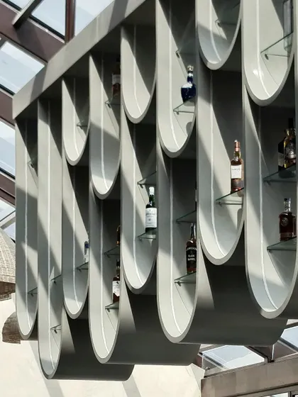 A daytime shot of the suspended bar display highlights its unique form and the way it interacts with sunlight. The design turns bottle storage into an art installation, visible from all angles of the restaurant.