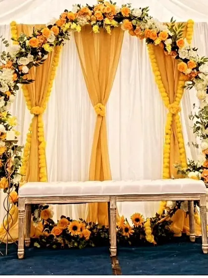 An elegant Haldi backdrop with a floral arch of yellow and white roses over draped yellow curtains. The use of sunflowers at the base adds a bright and cheerful element to the overall sophisticated design.