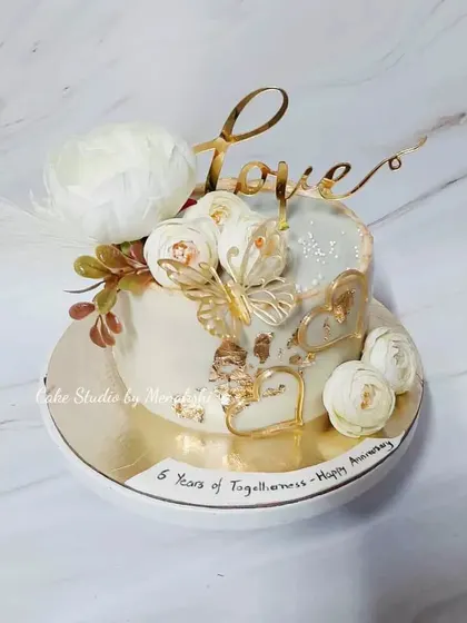This anniversary cake in white and gold is all about love. It's a no-fondant design decorated with white flowers, golden hearts, and a butterfly for a touch of delicate charm.