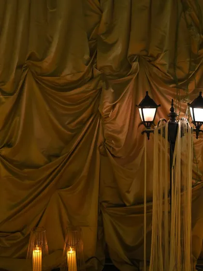 An atmospheric shot of a vintage-style lamppost set against a backdrop of draped golden fabric. The warm lighting and rich textures create a dramatic and sophisticated mood.