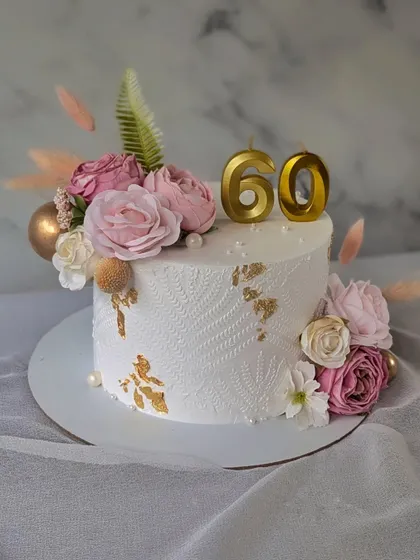An elegant and classy cake for a 60th birthday. This design features a delicate stencil pattern on white buttercream, accented with gold leaf and a beautiful arrangement of pink and white flowers.