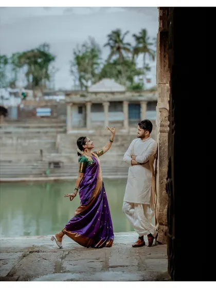 A playful and artistic shot of the bride dancing for the groom, who leans against a pillar by the temple pond, creating a scene straight out of a movie.