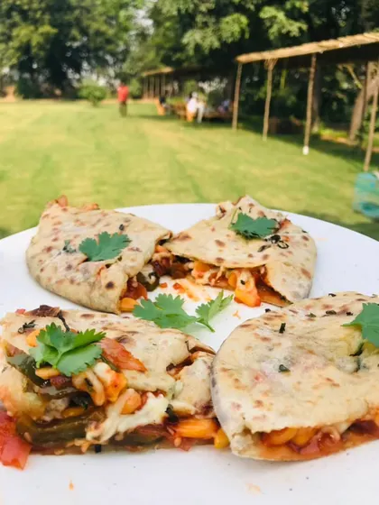 A plate of our delicious stuffed flatbread, garnished with fresh coriander, served in the open green space of our farm.