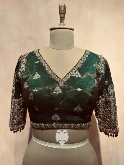 An Eden green tissue brocade blouse with a deep V-neckline and sleeves featuring intricate elephant and floral motifs.