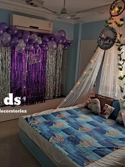 A full view of a bedroom decorated for a special occasion. We combined a purple and silver balloon backdrop with a beautiful fairy light canopy over the bed, creating a cozy and celebratory space.
