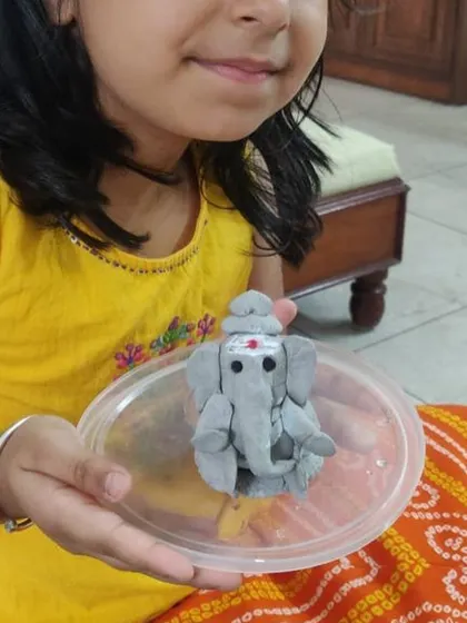 A child proudly displays her colorful clay Ganesha. The freedom to choose colors and shapes makes the activity a true expression of her creativity.
