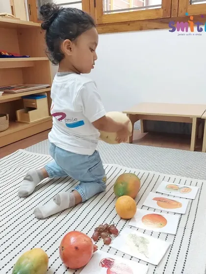 A toddler carefully examines a melon before placing it on the mat. We encourage children to use all their senses to explore the materials in their environment.