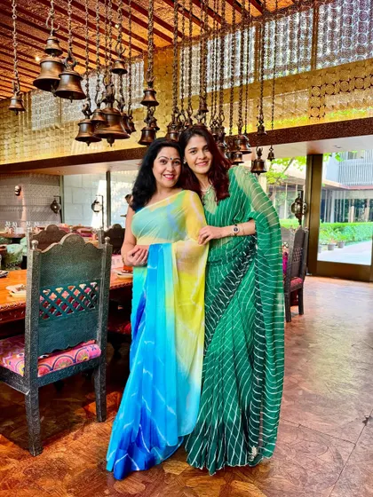Celebrating Teej with family. I'm wearing a green leheriya saree, a traditional Rajasthani print, which feels festive and appropriate for the occasion. My mother complements the look in her beautiful blue and yellow saree.