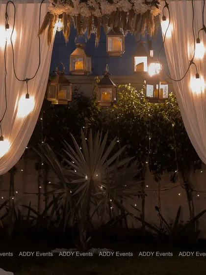 This dreamy bohemian arch, draped in soft white fabric and illuminated by hanging lanterns and Edison bulbs, serves as a perfect photo backdrop or ceremony focal point. The floral tie-backs add a touch of rustic elegance.