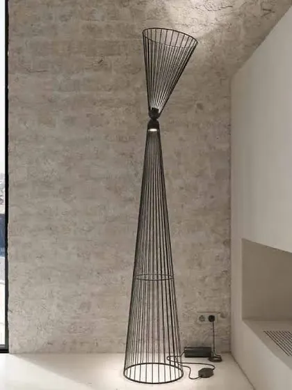 The Ikonika floor lamp against a textured concrete wall, its clean, geometric lines creating a striking contrast with the raw material of the wall.