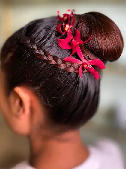 This braided bun, accented with vibrant red orchids, showcases a fusion of textures and colors. The sleek braid provides structure, while the delicate flowers add a touch of exotic elegance, making it a versatile choice for festive occasions.