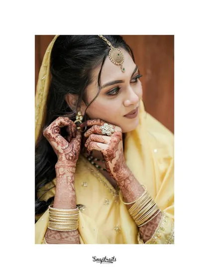 A duplicate of a candid moment of the bride adjusting her earring, her intricate henna and traditional jewelry on full display.