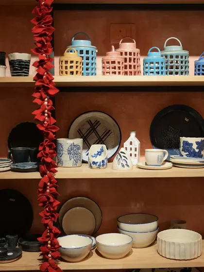 A view of our studio shelves, beautifully stocked with a colorful array of finished handmade pottery. You can see lanterns, plates, bowls, and mugs, showcasing the breadth of our work.
