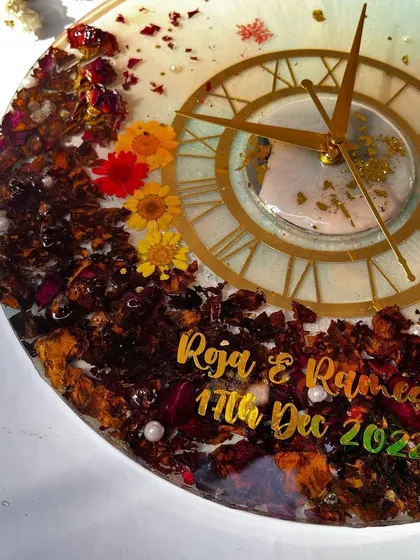 A close-up of a 12-inch clock with a mix of colorful preserved flowers. The bright yellow and red flowers really stand out against the darker rose petals.