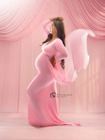 A graceful and artistic pose in a pink gown against a draped pink backdrop. The flowing fabric creates a sense of movement and elegance.